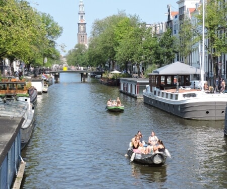 Twee boten die langs aangemeerde boten varen op de Amsterdamse grachten.