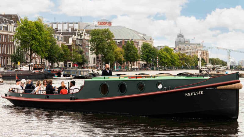 Klassieke sleepboot op de Amsterdamse grachten met een groep mensen en een schipper.