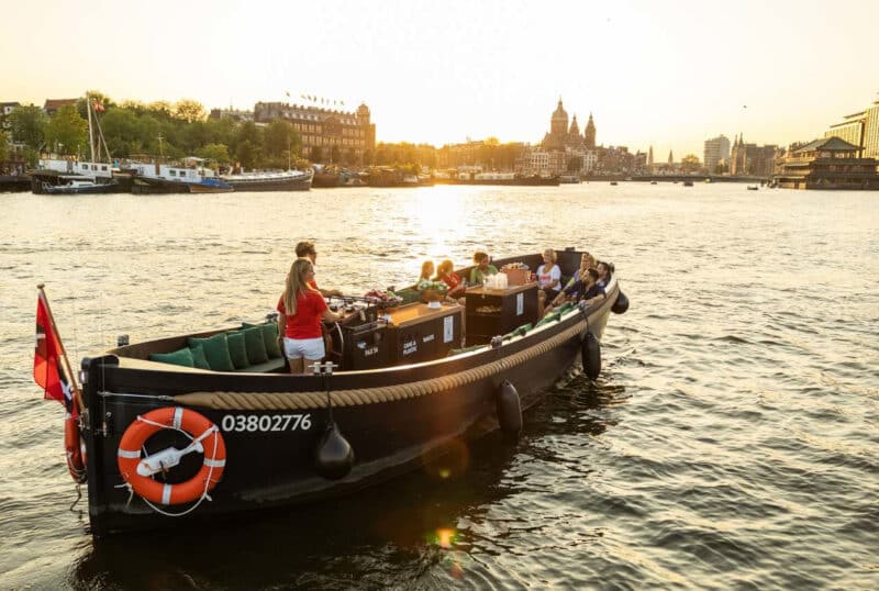 Open boot met schipper tijdens zonsondergang op de Amsterdamse grachten.
