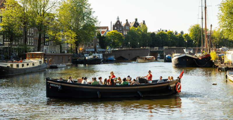 Een groep mensen tijdens een privé rondvaart op een open boot op de Amsterdamse grachten.
