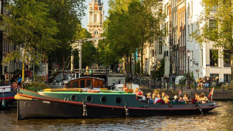 Klassieke sleepboot tijdens zonsondergang op de Amsterdamse grachten met een groep mensen.
